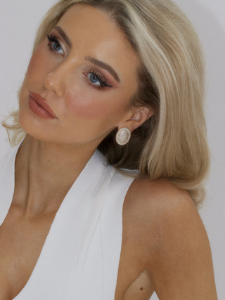 Gold plated Gigi earrings encrusted in sparkly cz stones, worn by a model in a white blouse