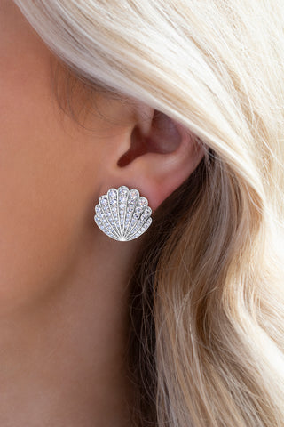 Muriel shell-shaped stud earrings in sterling silver with white gold plating and pavé-set cubic zirconia, worn in a model's ear and shot close up