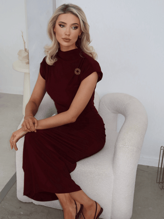 Model wearing the Amanda Chocolate brooch and matching earrings, styled on a burgundy dress and seated on a cream boucle chair
