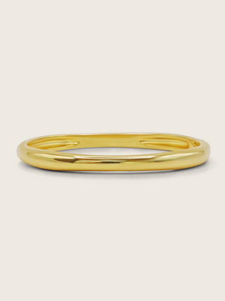Christy bangle in 14k gold plating with smooth, polished finish on neutral background