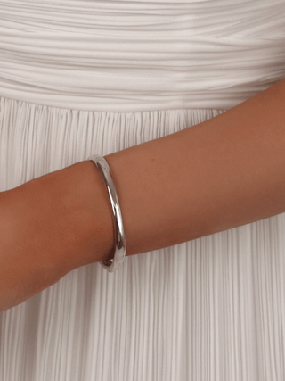 Christy bangle in sterling silver with premium White Gold plating, styled on wrist with pleated white dress