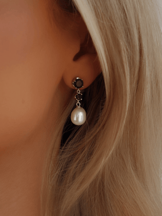 Close-up of Clarissa earrings with white gold plating, deep blue gemstones, and freshwater pearl drops, worn by model with blonde hair, elegant styling for formal occasions