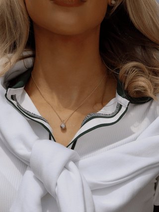Gold pavé tennis ball pendant necklace styled with green and white tennis outfit