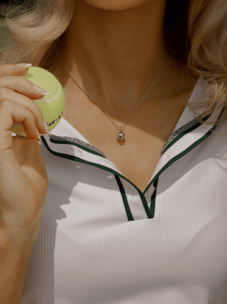 Model wearing white gold semi pavé tennis ball necklace paired with tennis-inspired outfit