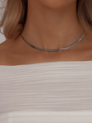 Dakota herringbone necklace in White Gold finish, styled on model with pleated off-shoulder white top