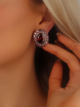 Close up of model wearing Diana earrings in white gold with deep wine coloured oval stone and cubic zirconia halo