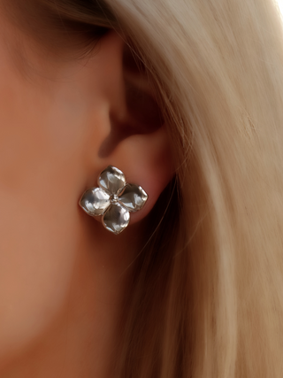 Close-up of Florence hydrangea-shaped stud earrings in sterling silver with white gold plating, showing the polished sculptural petals worn elegantly on the model’s ear for a refined, understated look.