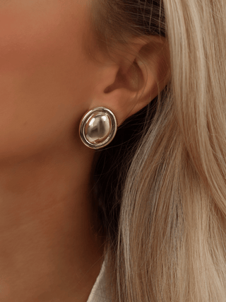 Gold plated Gigi oval stud earrings worn on model. Bold, polished dome-style design with a smooth, sculptural finish for statement styling.