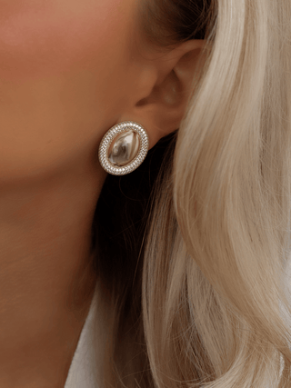 Gold plated Gigi semi pavé oval stud earrings with clear CZ stones, worn on model. Polished dome centre framed by sparkling pavé crystal border.