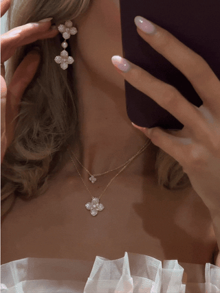 Mirror selfie GIF showing layered gold hydrangea necklaces and matching pearl drop earrings in light pink, styled with soft tulle for a dreamy romantic aesthetic