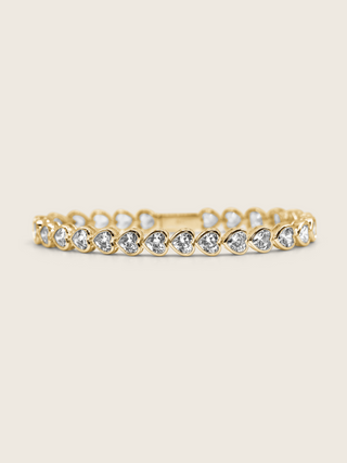 Gold plated heart tennis bracelet with bezel-set heart-cut cubic zirconia stones, elegant and romantic with a warm-toned finish, photographed on a neutral background
