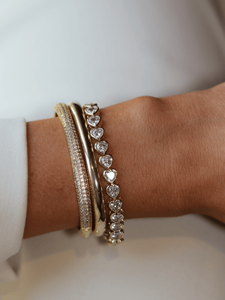 Juliette bracelet in gold with heart-shaped CZ stones, worn stacked with bangles on wrist for a radiant, layered look with refined sparkle