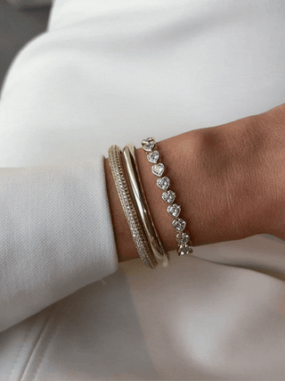 GIF of stacked gold bracelets featuring heart-shaped CZ Juliette tennis bracelet on model's wrist, reflecting movement and sparkle with soft luxury styling