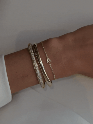 Shimmering GIF of stacked wrist featuring gold Love Letter bracelet with ‘A’ CZ initial charm, styled with contrasting bangles for an elegant mixed-texture finish