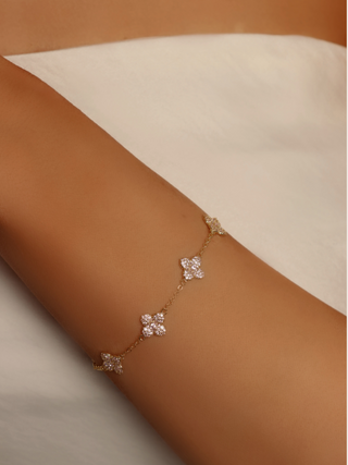 Gold hydrangea charm bracelet with light pink CZ stones, worn on model’s wrist with a white dress - a feminine, layered jewellery look