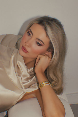 Model reclining in satin dress wearing gold plated pavé slim Christy bangle stacked with other bracelets. Soft glam jewellery styling.