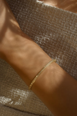 Gold plated pavé slim Christy bangle worn on wrist with natural sunlight and shadows. Dainty half-set CZ bangle for elegant everyday styling.