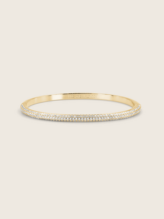 Gold plated pavé slim Christy bangle on white background. Half-set CZ stacking bracelet with slim profile and sparkly finish.