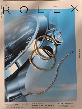 Gold plated slim Christy bangle styled with other bangles on Rolex magazine. Flatlay of CZ pavé bracelet with luxury accessories.