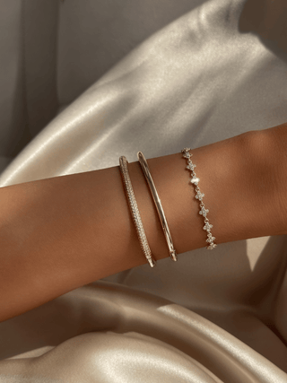 Plain gold plated slim Christy bangle stacked with pavé Christy bangle and Micro Hydrangea Bracelet on satin background. Minimalist gold bracelet layering for refined everyday styling.