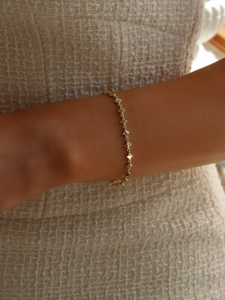 Gold plated micro hydrangea bracelet on model's wrist, paired with a cream dress, showcasing the elegant design of the chain bracelet.