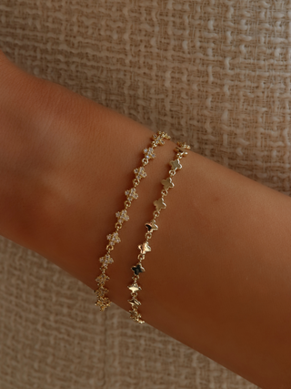 Gold plated micro hydrangea bracelet stacked with sparkly version on model's wrist, paired with a cream dress, highlighting the elegant layered look of the chain bracelets.