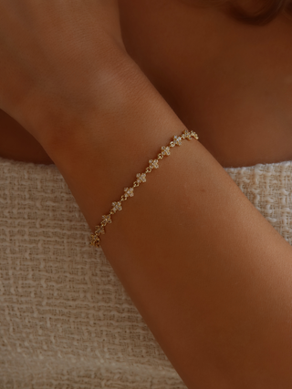 Close-up of gold plated pavé bracelet on model's wrist, with a cream dress in the background, showcasing the sparkling detail of the chain bracelet.