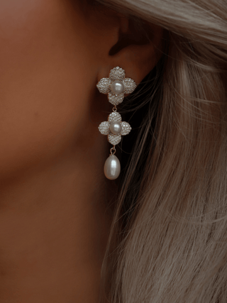 Model wearing 14k gold plated floral drop earrings with freshwater pearls and pavé CZ detailing