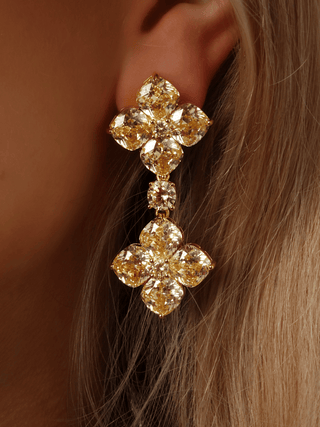 Close-up of gold-plated 5cm drop earrings with double lemon CZ hydrangea clusters and central cushion-cut connector, worn on model’s ear