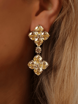 Close-up of white gold-plated 5cm drop earrings with double lemon CZ hydrangeas and centre connector, shown worn on model’s ear