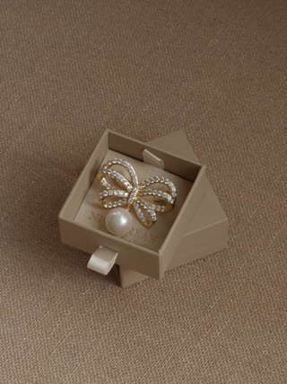 Meredith bow-shaped brooch with sparkling crystals and a shell pearl, elegantly presented in brand packaging, ideal for weddings, summer events, and special occasions.