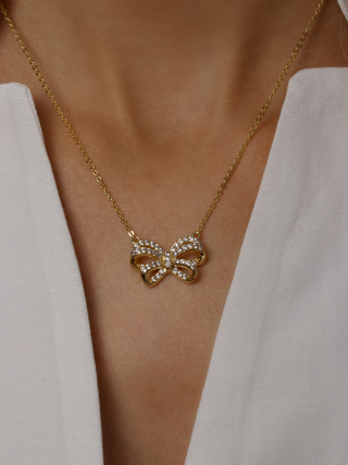 Meredith Bow Necklace in 14k gold plating with crystal pavé bow pendant, worn on model with white blouse