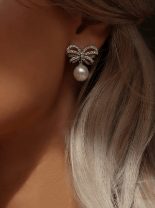 Close-up of white gold bow earrings with CZ stones and shell pearl