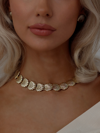 Closeup of Muriel necklace on model’s neck, featuring overlapping shell designs in gold