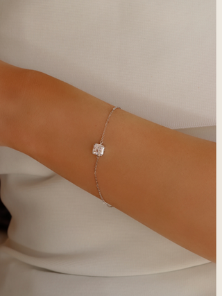 Close-up of the Regina bracelet worn with a white dress, highlighting the minimalist square CZ stone and fine sterling silver white gold plated chain for a sophisticated, understated wrist accessory.