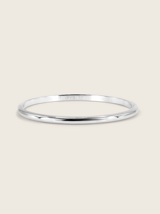White gold plated slim Christy bangle on white background. Sleek and simple bangle with polished surface, perfect for minimalist jewellery styling.