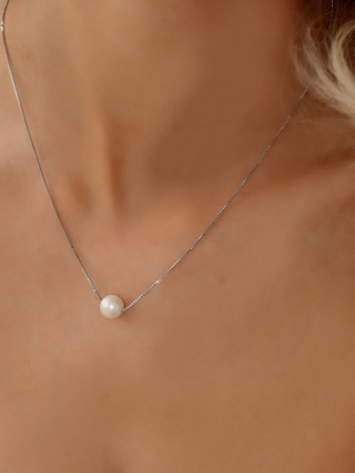 White gold plated necklace with single round freshwater pearl, minimalist design shown on model’s neck