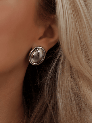 White gold plated Gigi oval stud earrings worn on model. Smooth sculptural dome design with a polished finish for bold, minimalist styling.