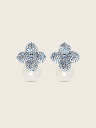 White gold plated hydrangea flower earrings with light blue cubic zirconia and shell pearl drop on white background. Sparkly floral stud earrings