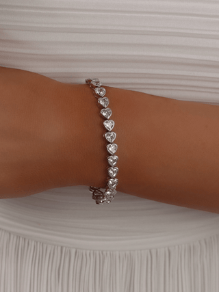 White gold plated bracelet with heart-shaped CZ stones, styled on model with pleated white dress - perfect for formal occasions or bridal elegance