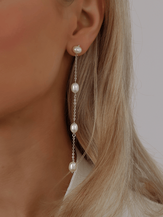 White gold plated Leah freshwater pearl drop earring with four pearls linked on a fine chain, worn on model. Elegant long dangle earring for refined minimalist styling.