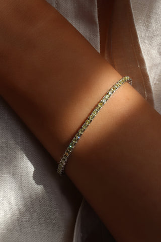 Artistic close-up of the Xanthe tennis bracelet on the model’s wrist, illuminated by a slit of light to showcase the vibrant yellow CZ stones bezel-set in white gold plating, radiating sophisticated golden sparkle with every movement.