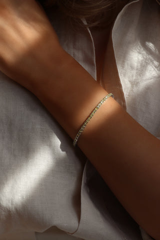 Elegant view of the Xanthe tennis bracelet worn on the model’s wrist, featuring vibrant yellow CZ stones set in white gold plating, with a soft white dress background enhancing the bracelet’s sophisticated, sunlit sparkle.