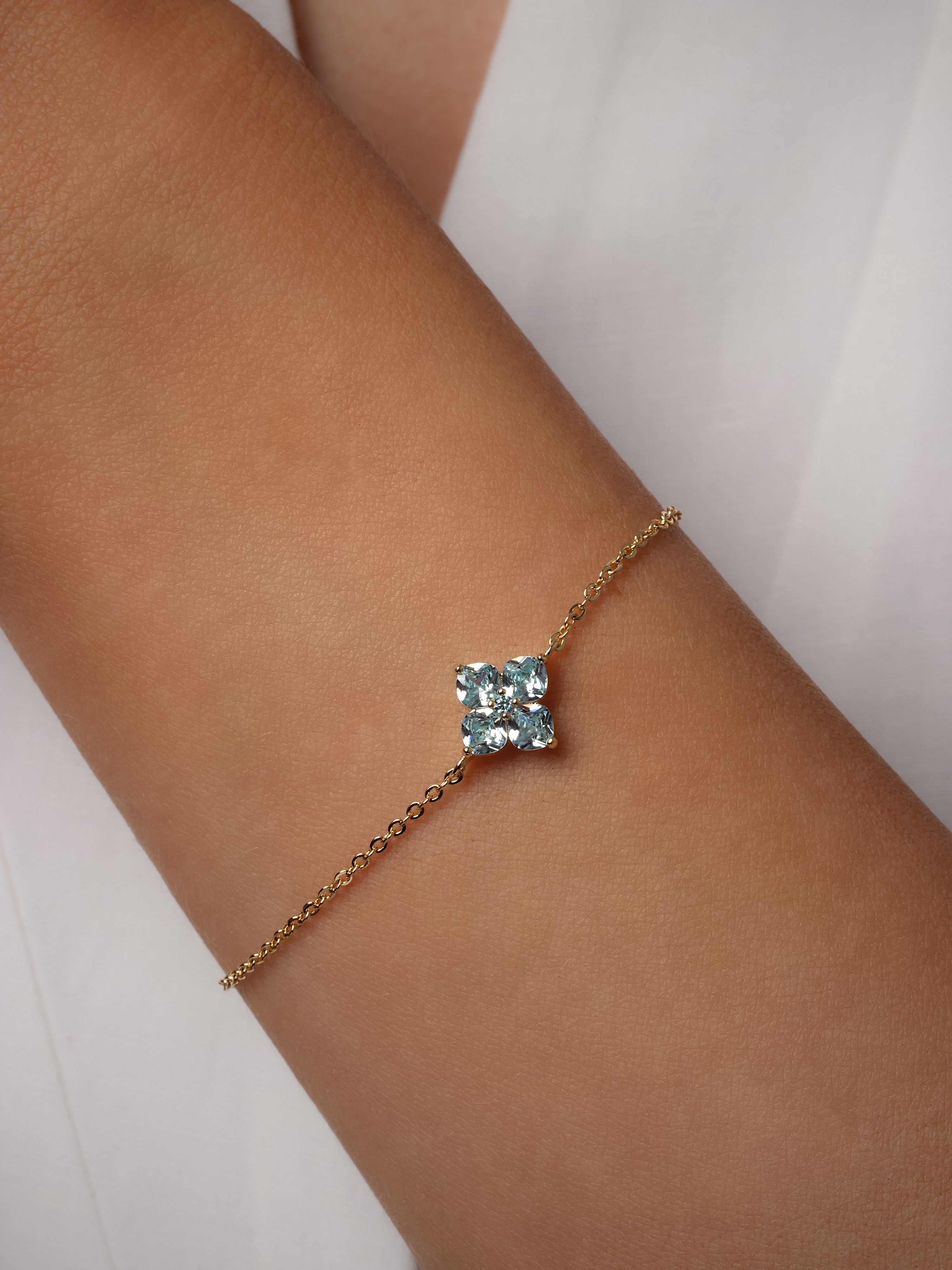 Blue mini crystal hydrangea bracelet with a fine gold plated chain, catching the light on a model's wrist close up