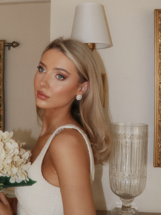 Model in white dress holding flowers, wearing pearl stud earrings