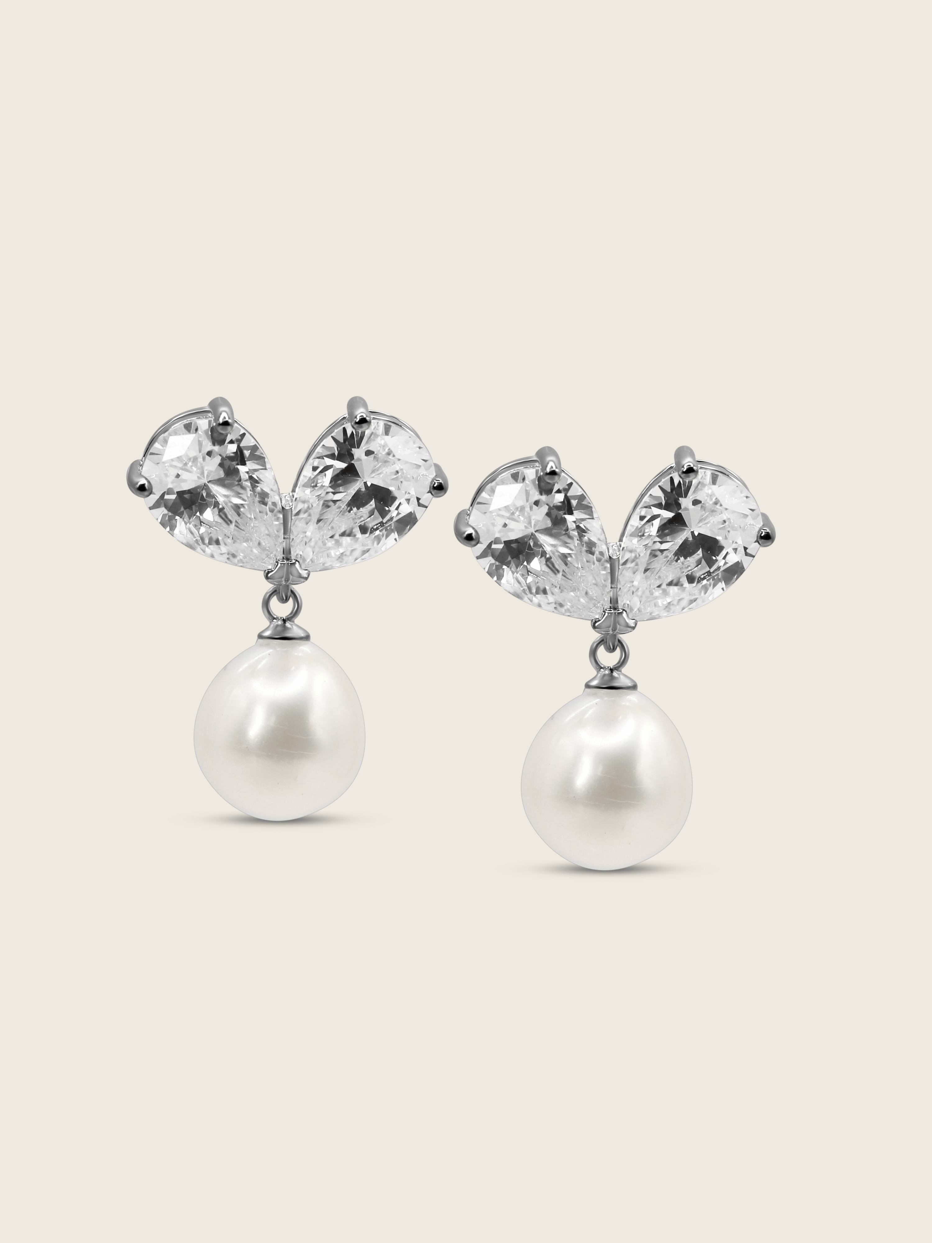 The Adore Earrings featuring two clear pear-cut CZ stones and a single freshwater pearl, set in sterling silver with white gold plating, displayed against a clean white background.