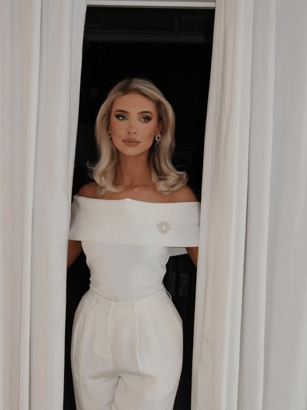 Model wearing Amanda Brooch in 14k gold plating with clear crystal cubic zirconia stones and matching Amanda Earrings, styled on white outfit