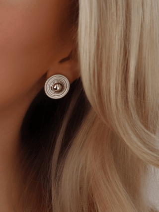 Athena stud earring in sterling silver with white gold plating, featuring a raised domed centre and concentric circular design, vintage-inspired mid-century jewellery shown worn on a model with blonde hair.