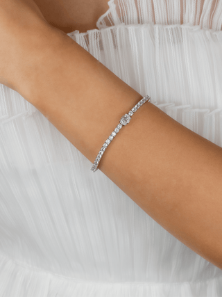 white gold Aurelia bracelet with an oval cut clear stone, worn on a model with a pleated white dress, showing sparkle and clarity