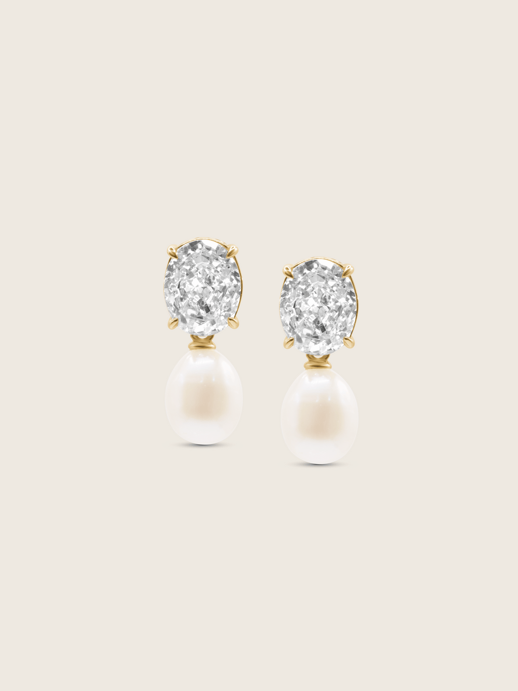 Flatlay of Aurelia earrings with clear CZ stones and freshwater pearl drops in 14k gold plating on neutral background
